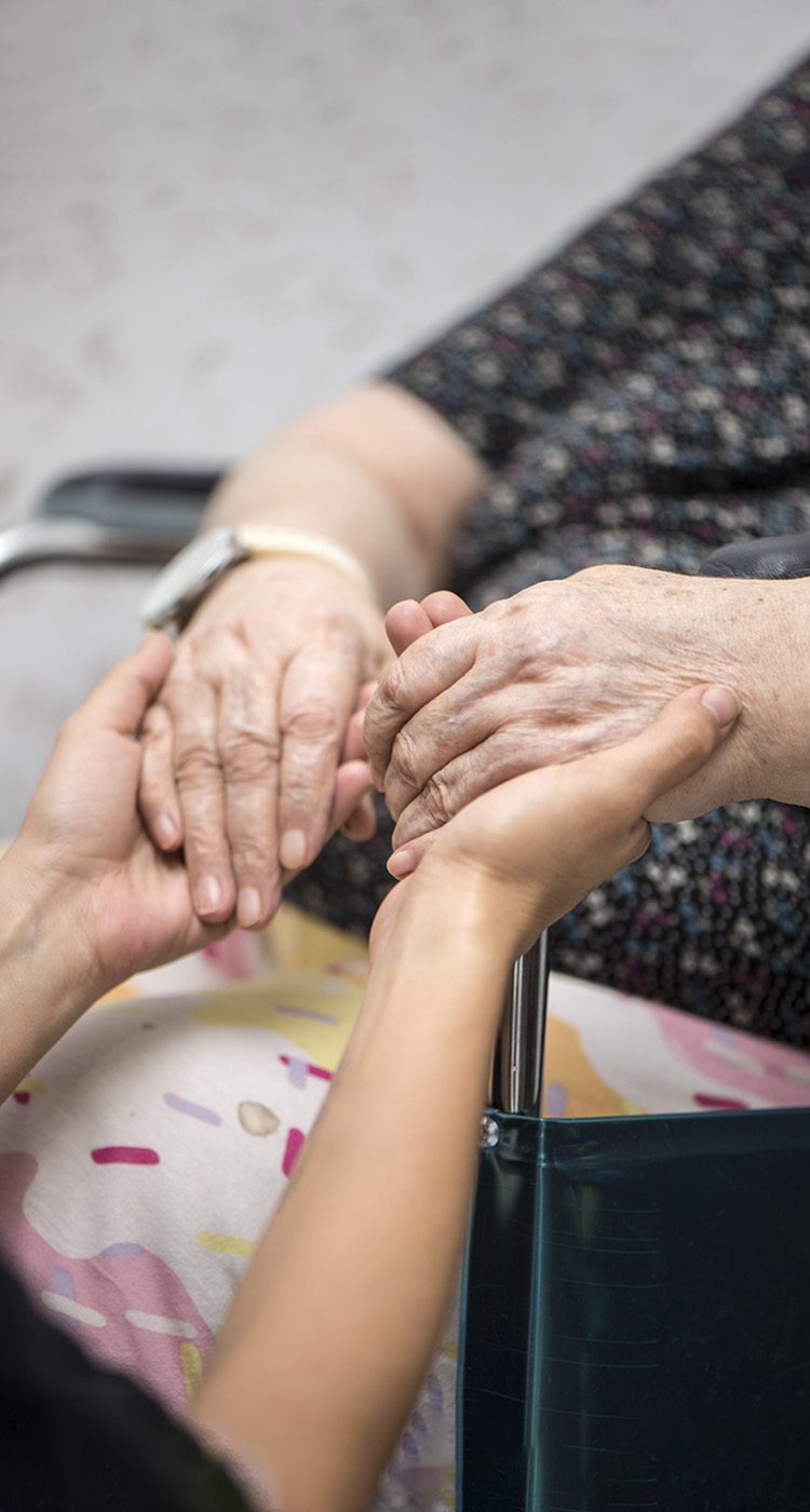 Caregiver holding elderly woman's hands in wheelchair