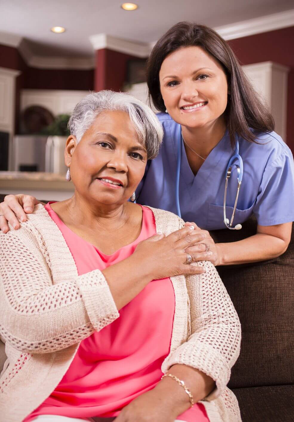 Older woman sitting with a female nurse smiling behind her.